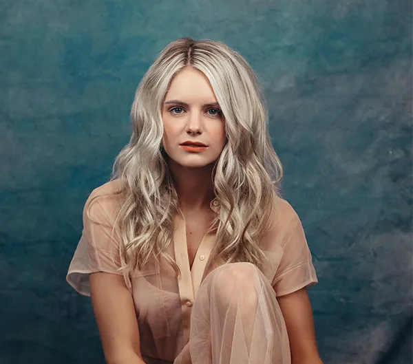 A woman with long, wavy blonde hair posing against a blue background, showcasing a beautiful hairstyle created at the hair salon